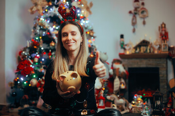 Happy Christmas Girl Holding a Piggy Bank Making Thumbs-up Gesture. Cheerful person enjoying the...
