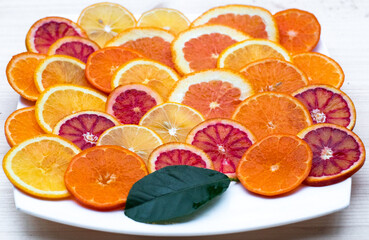 A plate of sliced oranges and lemons decorated with green leaf