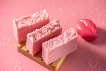 Cute pink pieces of handmade natural soap on a wooden soap dish on a pink background. Modern and safe cosmetic products for skin care and interesting hobby