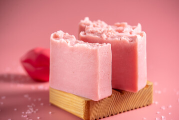 Cute pink pieces of organic eco soap on a soap dish made of natural wood on a pink background. Concept of modern and safe cosmetic products for skin care