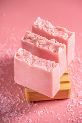 Cute pink pieces of handmade natural soap on a wooden soap dish on a pink background. Modern and safe cosmetic products for skin care and interesting hobby