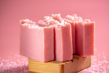 Cute pink pieces of handmade natural soap on a wooden soap dish on a pink background. Modern and safe cosmetic products for skin care and interesting hobby