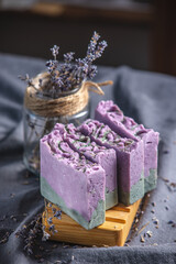 Pieces of natural lavender handmade soap on a wooden soap dish and on a dark fabric background with dry flowers. Concept of organic cosmetics, a useful and interesting hobby, a beautiful postcard