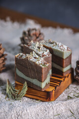 Fragrant pieces of natural coniferous soap handmade on a wooden soap dish, surrounded by cones and needles on a background of fabric. Atmospheric winter postcard