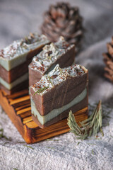 Fragrant pieces of natural coniferous soap handmade on a wooden soap dish, surrounded by cones and needles on a background of fabric. Atmospheric winter postcard