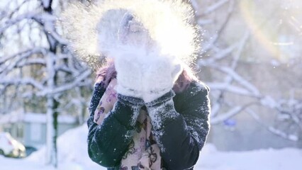 Smiling happy woman portrait blow snow from hands in gloves to camera. Beautiful playful girl enjoy Christmas New Year vacation outdoor have fun during winter vacation. Concept of happiness pleasure