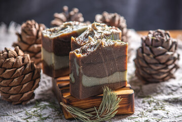 Fragrant pieces of natural coniferous soap handmade on a wooden soap dish, surrounded by cones and...