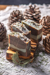 Fragrant pieces of natural coniferous soap handmade on a wooden soap dish, surrounded by cones and needles on a background of fabric. Atmospheric winter postcard
