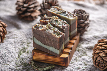 Fragrant pieces of natural coniferous soap handmade on a wooden soap dish, surrounded by cones and needles on a background of fabric. Atmospheric winter postcard