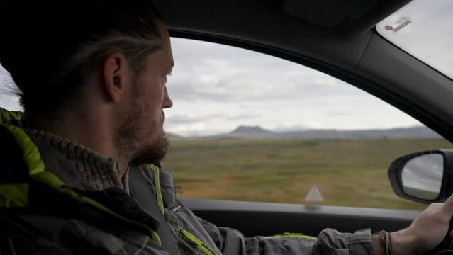 Sideways shot of caucasian man focussed driving the car in mountain landscape of Iceland.