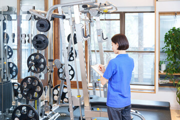 スポーツジムのトレーニングマシンを点検する女性スタッフ - obrazy, fototapety, plakaty