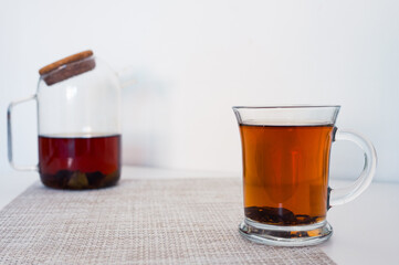 Black tea in a glass cup and glass teapot freshly brewed on a napkin with white background