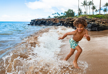 Smiling young African American boy running and playing at the beach while on a family vacation. Playing in the ocean waves having fun and being active
