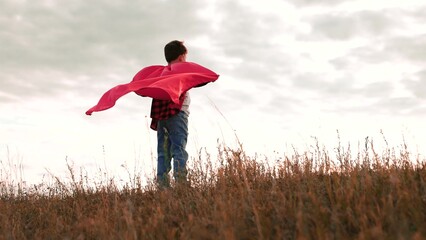 Boy stands in field extending arms wearing red raincoat in overcast weather