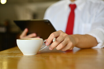 Closeup view business man hand holding a cup of black hot coffee and using digital tablet
