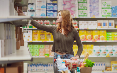 Woman doing grocery shopping and taking a product from a shelf