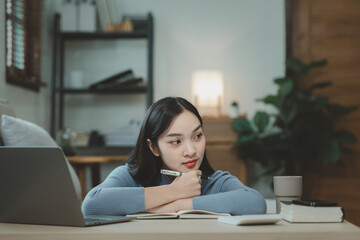 A student is sitting in the living room doing homework, Sitting and looking for information and making reports to send to teachers in the house, Recording various information In the book at apartment.