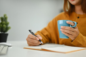 Young woman holding cup of hot tea and writing notes in personal daily planner