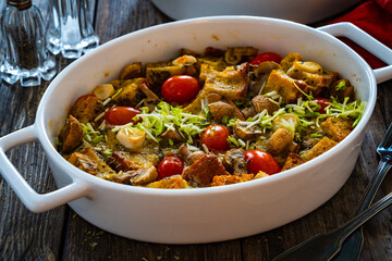 Bread casserole with mozzarella cheese, tomatoes and scrambled eggs on wooden table
