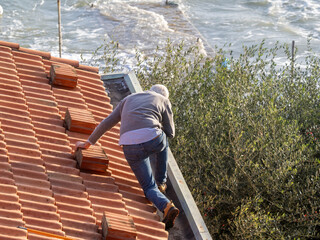 A man worker is cleaning a clogged roof gutter from dirt, debris and fallen leaves to prevent water...