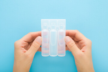 Woman hands holding and showing pack of transparent plastic ampoules with drug liquid on light blue table background. Pastel color. Medicine and healthcare. Closeup. Point of view shot. Top down view.