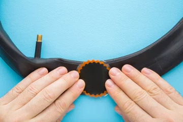 Foto op Canvas Man fingers gluing patch on dark black rubber deflated bicycle tube on pastel blue table background. Hole repair after nail, screw or other sharp things. Closeup. Point of view shot. Top down view. © fotoduets
