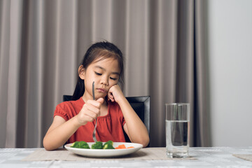 Little cute kid girl refusing to eat healthy vegetables. Children do not like to eat vegetables.