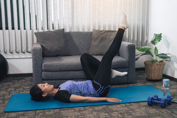 Asian woman practicing yoga at home while lying on a mat and stretching her legs.