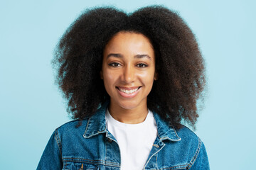 Portrait of successful smiling African American woman with curly hair looking at camera isolated on blue background 