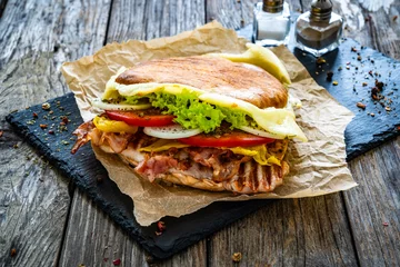 Fototapeten Big sandwich with grilled chicken breast and cheese and fresh vegetables on wooden table  © Jacek Chabraszewski
