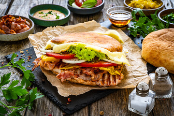 Big sandwich with grilled chicken breast and cheese and fresh vegetables on wooden table
