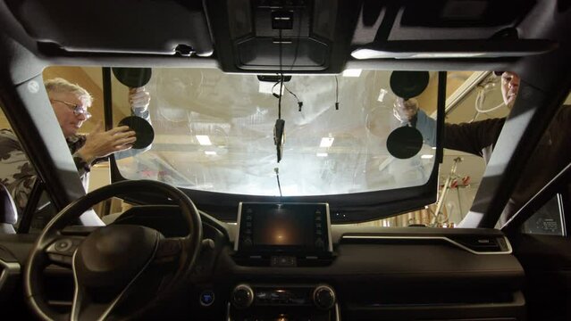 Two glass technicians fits new windscreen in place, view from inside car