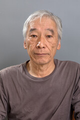 白髪混じりの60代の男性が、正面を向いているがほぼ無表情