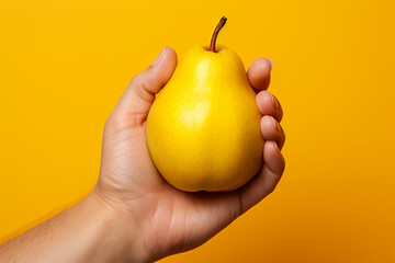 Close-up of a hand holding a pear on a yellow background