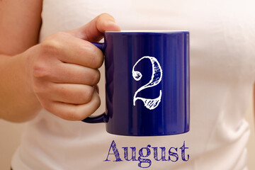 The inscription on the blue cup 2 august. Cup in female hand, business concept