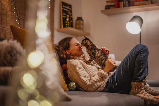Cozy at home with tabby cat, woman with her pet on sofa ay home in evening