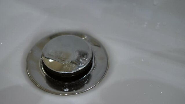 Close-up of water from a faulty faucet dripping into a sink with a drain plug. Outdated plumbing, broken faucet, leaking. Drinking water shortage