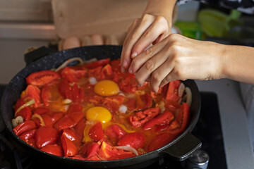  girl holds a chicken egg in her hand to break it. cooking scrambled eggs with tomatoes