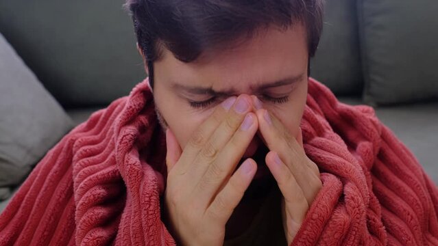 Young Caucasian man with runny nose holding paper napkins near face sitting at home. Sick guy caught bad cold showing symptoms of covid, or suffering from virus disease