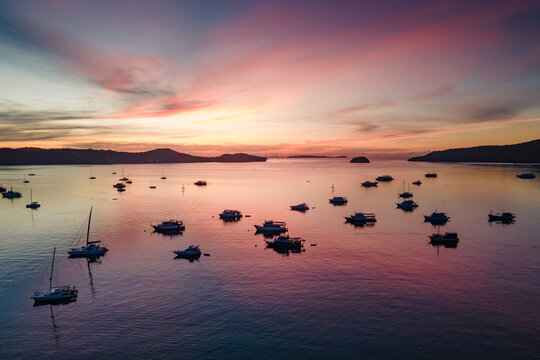 Aerial drone view of stunning sunrise at chalong bay with many tour boats and yachts anchored around. Colorful sky at dawn in Phuket, Thailand.
