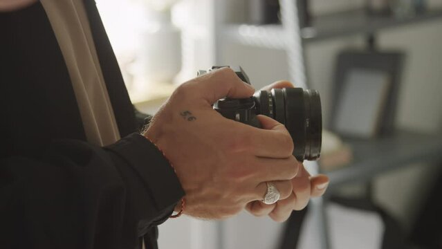 Close-up shot of hands of unrecognizable male photographer holding DSLR camera, adjustig focus and shooting photos of some object while working at studio