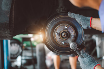 Auto mechanics in the garage replace brakes. A mechanic installing a car wheel while doing maintenance. A laborer changing the brake disk. Idea for putting in a brake disk. - obrazy, fototapety, plakaty