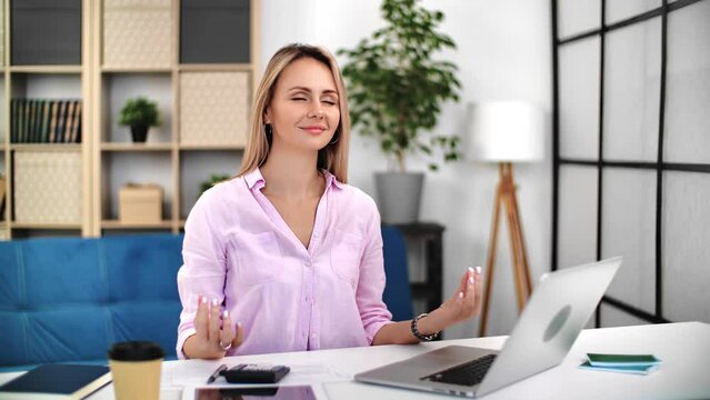 Smiling blonde business woman relaxing stress free at work office desk with yoga namaste hands