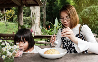 Asian mother takes her beautiful daughter to lunch of omelet at a restaurant. Leisure travel activities at the resort
