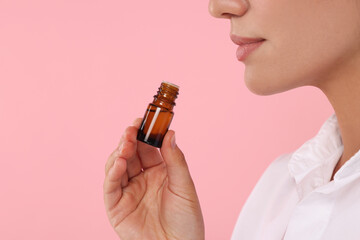Woman with bottle of essential oil on pink background, closeup