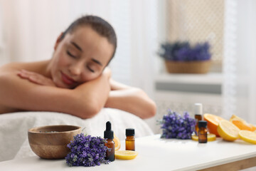 Woman relaxing on massage couch and bottles of essential oil with ingredients on table in spa salon, selective focus