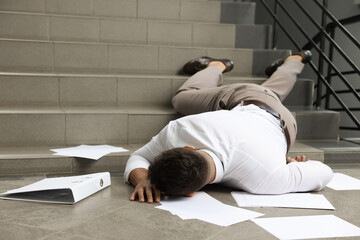 Unconscious man with scattered folder and papers lying on floor after falling down stairs indoors - obrazy, fototapety, plakaty