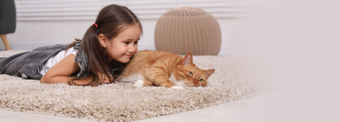Smiling little girl and cute ginger cat on carpet at home. Banner design with space for text