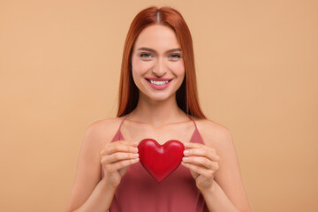 Beautiful happy woman with red heart on beige background