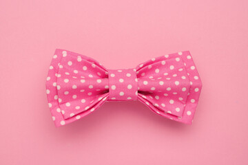 Stylish hot pink bow tie with polka dot pattern on color background, top view